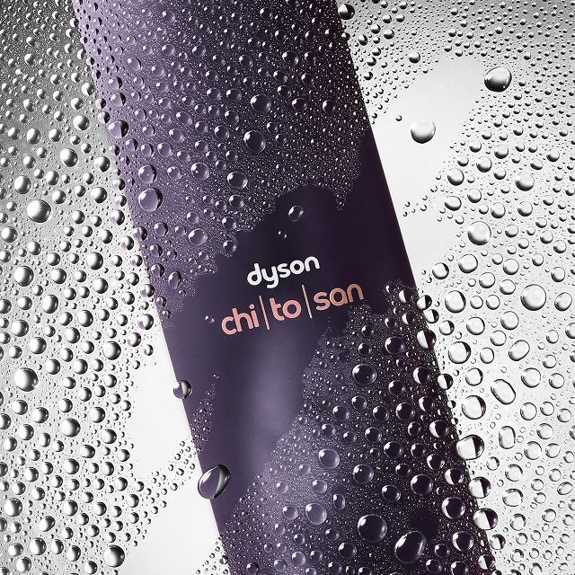 Dyson Chitosan Multi-use styling spray behind water droplets on a glass pane.