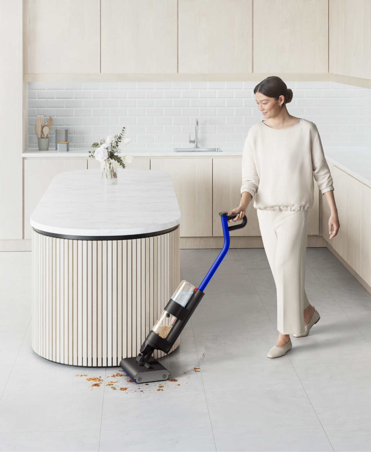 A woman cleaning a hard floor around a kitchen island with the Dyson WashG1 wet cleaner.