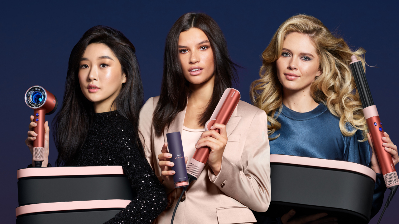 Three models holding Dyson Supersonic Nural hairdryer, Airstrait straightener and Airwrap i.d. multi-styler and dryer in Strawberry bronze. As well as the Dyson Chitosan styling range.